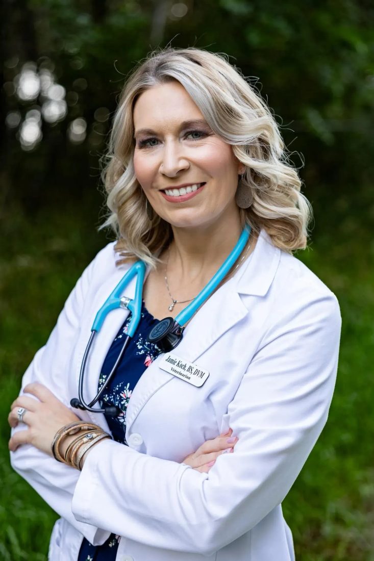 Blonde female veterinarian in white coat with stethoscope outdoors