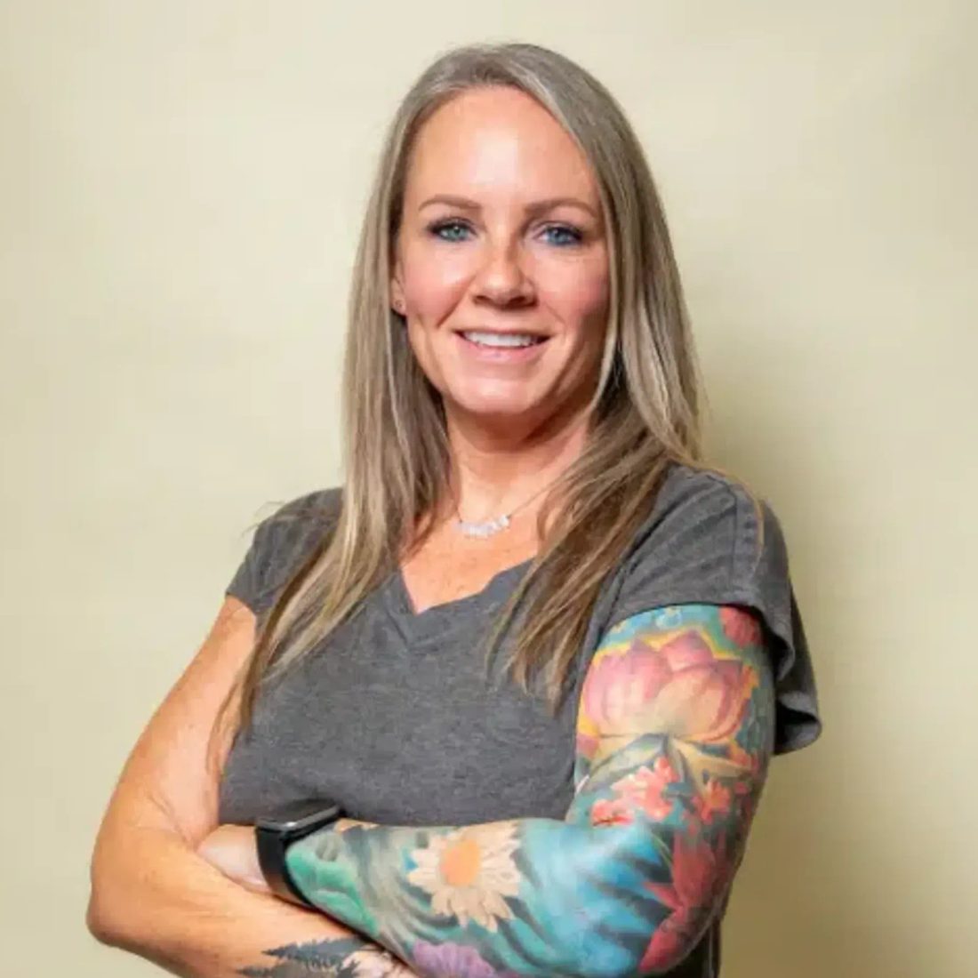 Smiling woman with tattooed arm in gray shirt against beige wall