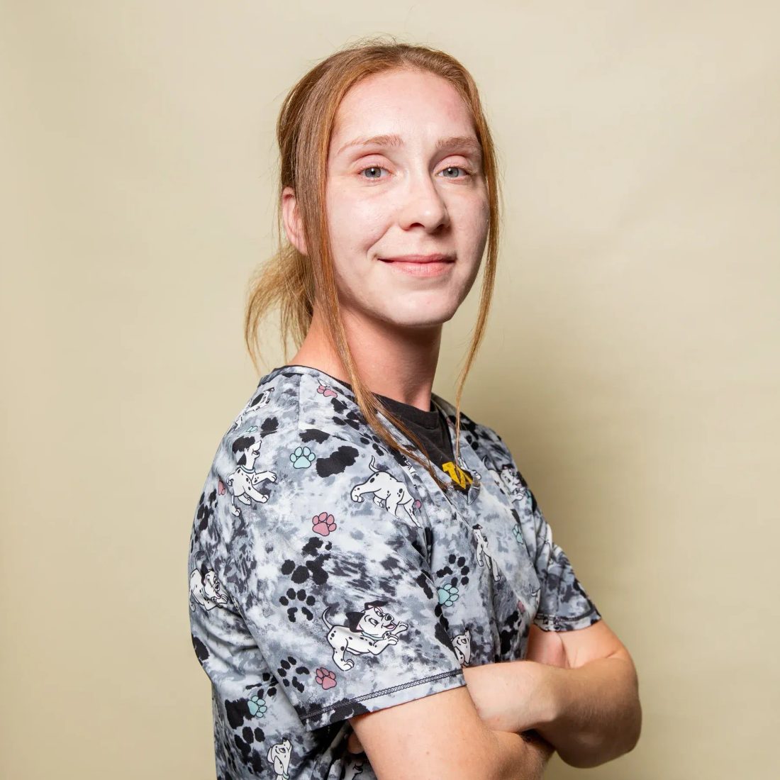 Woman in patterned scrub top with arms crossed smiling